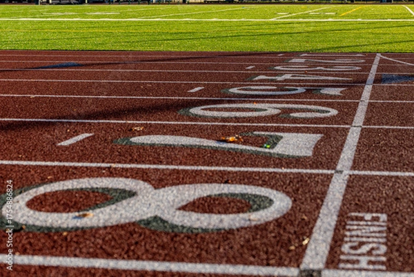 Obraz Close up photo of outdoor running track lanes with white numbers one, two, three, four five, six, seven, eight, 1, 2, 3, 4, 5, 6, 7, 8, with green shadow on a new red track with white lane lines.