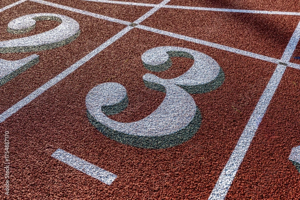 Obraz Close up photo of outdoor running track lane white number three, 3, with green shadow, on a new red track with white lane lines.