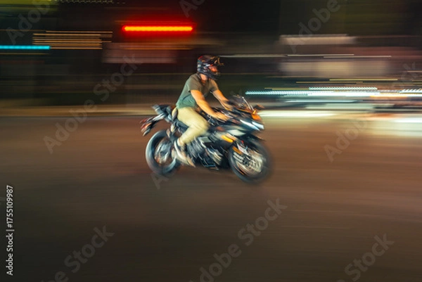 Fototapeta Biker riding motorcycle bike in night city. Blurred motion.