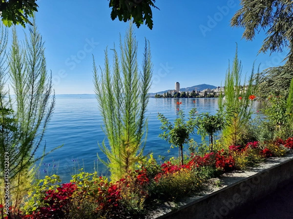 Fototapeta Sunny view of the Montreux promenade along Lake Geneva in Switzerland. Colorful flowerbeds, calm blue water, and a peaceful atmosphere capture the charm of this famous lakeside resort town.