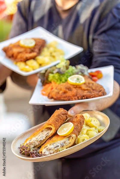 Fototapeta Waiter serving vegetarian and classic cordon bleu with potato salad and lemon garnish at an outdoor restaurant