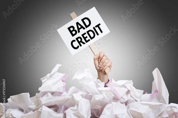 Fototapeta Bad credit  placard in hand with crumpled paper pile. Concept of bad financial situation.