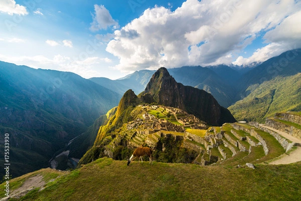 Obraz Machu Picchu oświetlone ciepłym światłem zachodzącego słońca. Szeroki kąt widzenia z tarasów powyżej z malowniczym niebem i rozbłyskiem słońca. Zjawiskowe miejsce podróży, cud świata. Region Cusco, Peru.