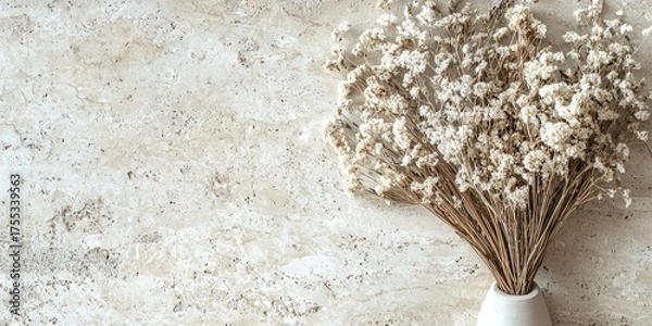 Fototapeta A bouquet of dried white flowers in a white vase on a textured stone surface.