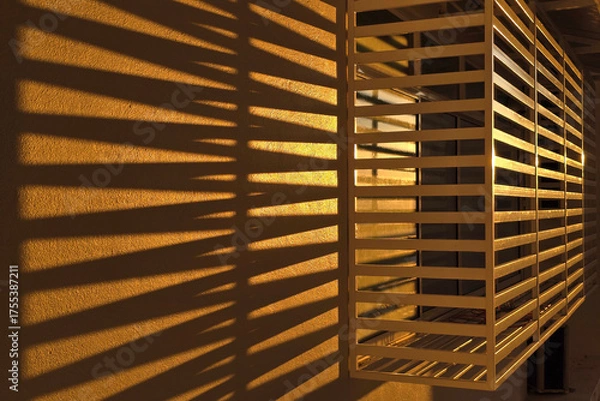 Obraz Golden Sunlight Casting Shadow Lines Through Window Grille on Wall