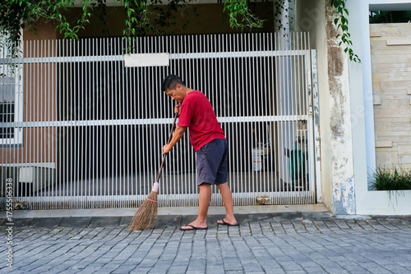 Fototapeta Man sweeping up the front yard with broomstick