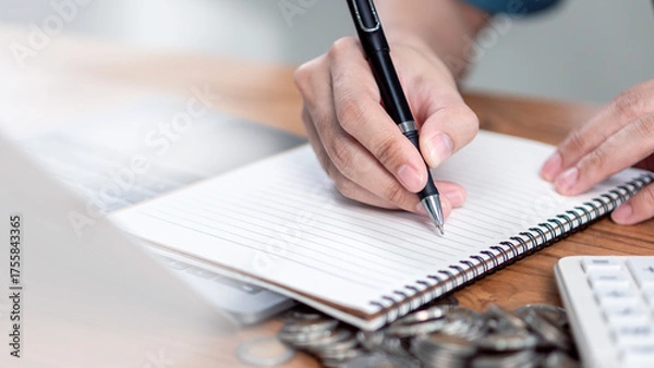 Fototapeta Personal finance planning and savings calculation at home , Close-up of a person writing in a notebook a calculator and stacked coins, representing personal finance planning, savings management.