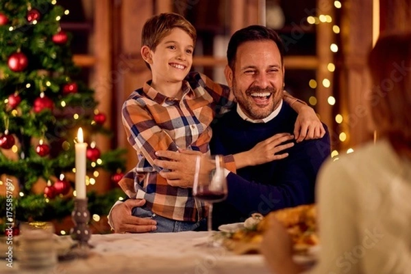 Fototapeta Happy Father and Son Share Warm Hug During Christmas Dinner by Tree and Candlelight Together