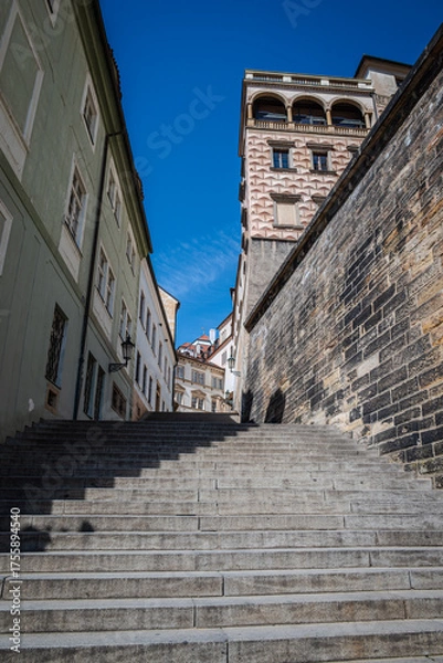 Fototapeta Stairs winding between buildings on a hill in Prague, Czech Republic, leading toward Prague Castle, photographed against a clear blue sky.