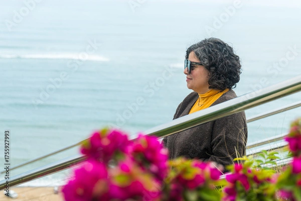 Obraz A woman is standing on a railing overlooking the ocean