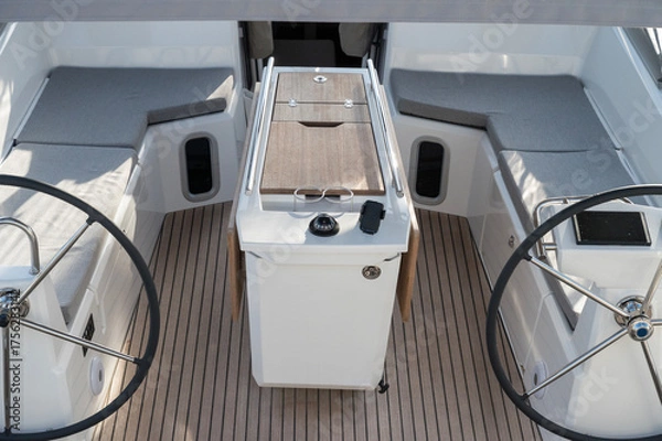 Fototapeta Sailboat with dual steering wheels, comfortable cabins with grey cushions, and wooden decking. Central table with compass and modern design, perfect for a comfortable and luxurious sailing experience.