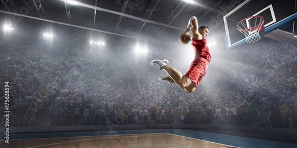Fototapeta Basketball player makes slam dunk on big professional arena. Player flies through the air with the ball. Player wears unbranded clothes.