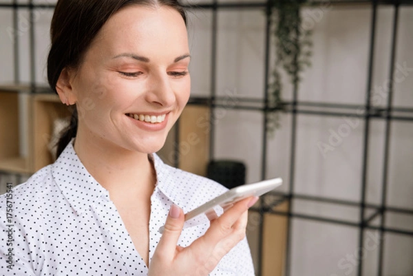 Obraz Young woman in white blouse talking on smartphone in office.