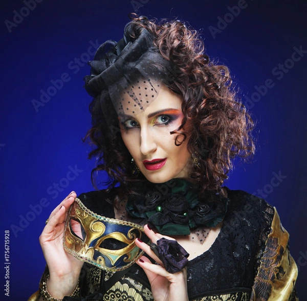 Obraz Portrait of smiling woman with artistic make-up holding mask over blue background.