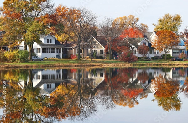 Fototapeta Autumn in a city background. Fall cityscape with private houses neighborhood along a pond. Colorful trees and houses reflected in a water. Midwest USA, Wisconsin. Classic american middle class homes.