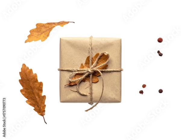 Obraz A square wrapped present, tied with twine and a dried leaf, resting with leaves and peppercorns