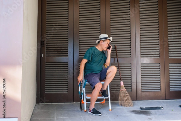 Fototapeta Man sitting on folding ladder answering a phone call during housekeeping