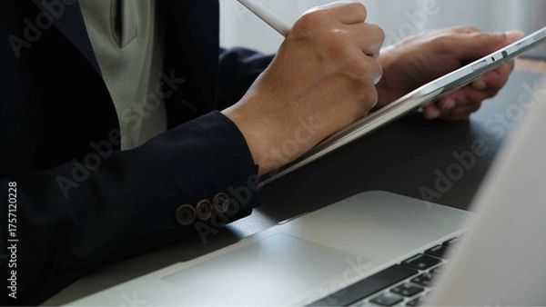 Fototapeta Business professional writing on digital tablet beside laptop in modern office workspace