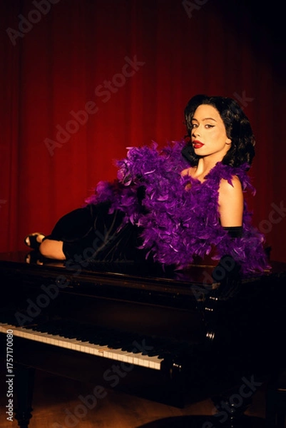 Fototapeta Performing artist in a purple feather boa poses on a grand piano with red curtains in the background during a glamorous evening event