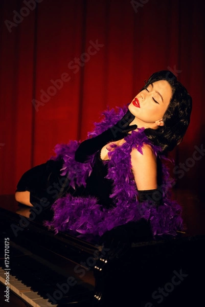 Fototapeta Performing artist in a purple feather boa poses on a grand piano with red curtains in the background during a glamorous evening event
