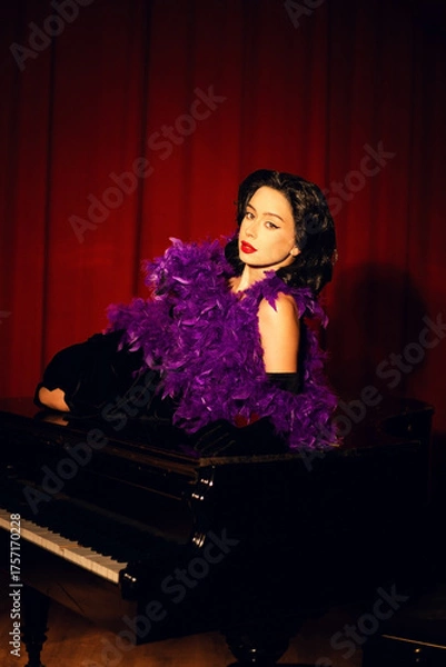 Fototapeta Performing artist in a purple feather boa poses on a grand piano with red curtains in the background during a glamorous evening event