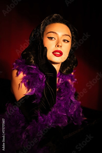 Fototapeta Performing artist in a purple feather boa poses on a grand piano with red curtains in the background during a glamorous evening event
