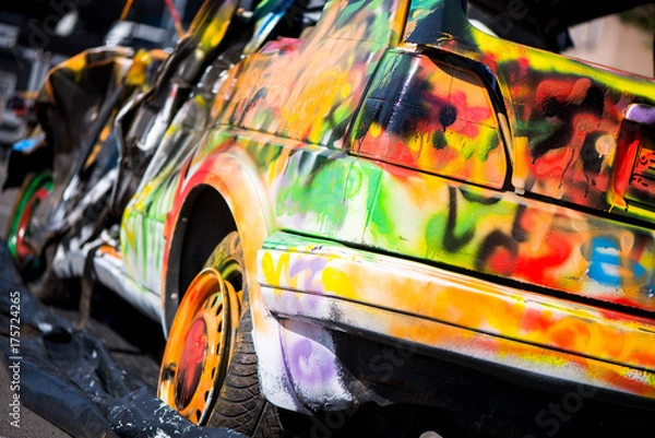 Obraz Macro shot of a colorfully painted car, an old crashed, damaged car wreck. Kids are having fun, making drawings and graffiti art, paint on wreck and tires with green, red, orange, yellow, blue colors