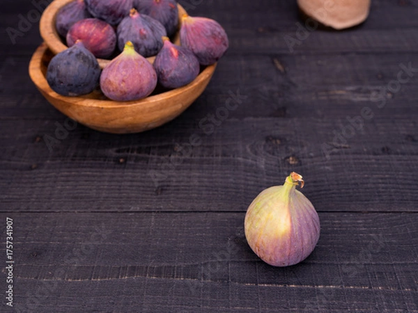 Obraz Fresh figs displayed on a black wooden table with one in front and more in wooden bowls, rustic and moody composition with vase in background