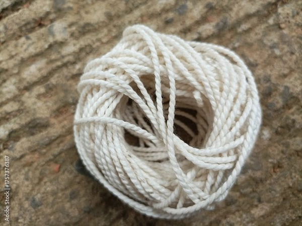 Fototapeta ball of string, A white yarn ball placed on a rough concrete surface under natural light, showing fine texture, soft tones, and aesthetic composition in close-up view.