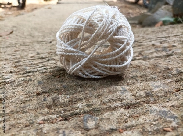 Fototapeta A white yarn ball placed on a rough concrete surface under natural light, showing fine texture, soft tones, and aesthetic composition in close-up view.