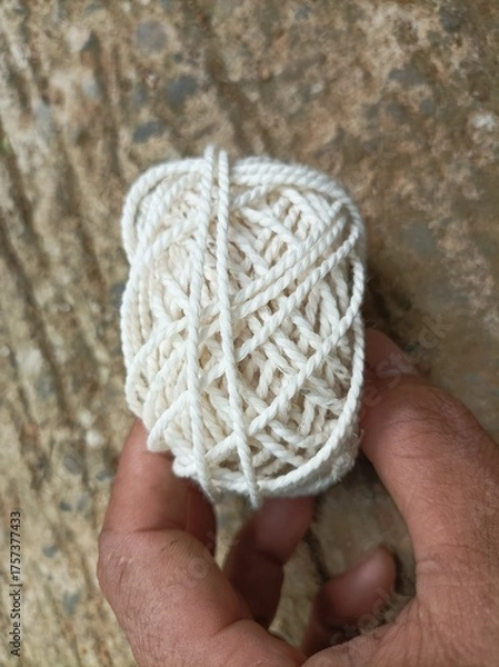 Fototapeta A white yarn ball held in a human hand with a natural background, showing fiber texture and soft details under warm natural light.