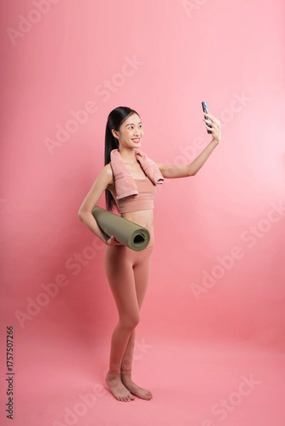 Obraz Woman in sportswear takes a selfie with a rolled-up mat against a pink background