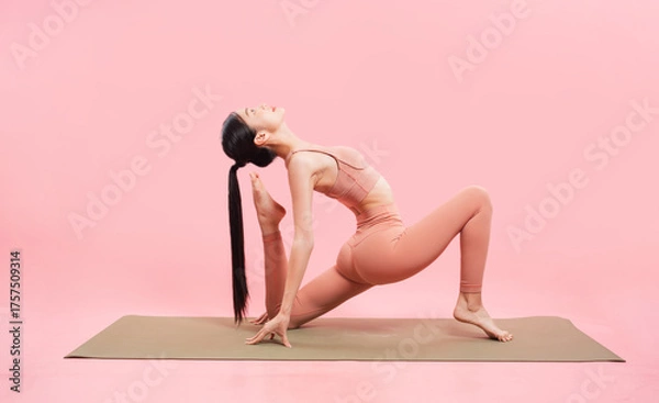 Obraz Woman in peach activewear does yoga on a light brown mat against a pink backdrop with ease