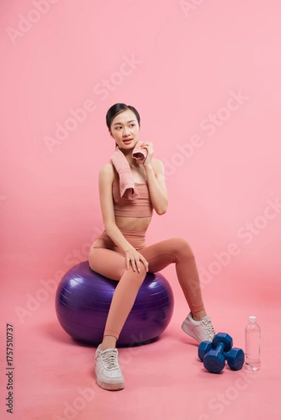 Fototapeta Fitness enthusiast rests on a balance ball after her workout on a vibrant pink backdrop