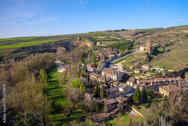 Obraz A picturesque view overlooks the Segovia Templar Church of Vera Cruz in a hilly valley, surrounded by a small village of brown-roofed houses below