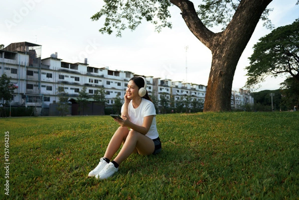 Fototapeta Woman relaxing in park listening to music