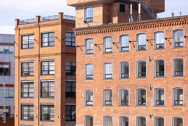 Obraz Historic red brick industrial building with large windows in an urban environment. Industrial style architecture with modern renovations under a clear sky