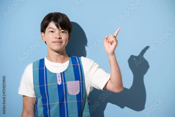 Fototapeta エプロンを着て指差しのポイントポーズをする男性　保育士・介護士などのイメージ　水色背景