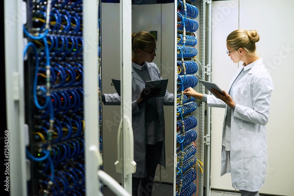 Fototapeta Portrait of young woman wearing lab coat working with servers in supercomputer research center, copy space