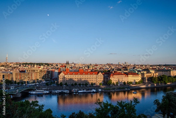 Fototapeta Evening sunlight bathes Prague Old Town, Czech Republic, with the Vltava River below and the moon rising in a clear sky- Horizontal