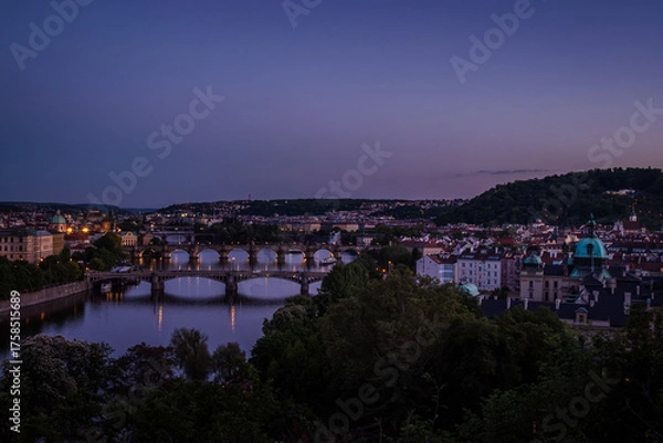 Fototapeta Twilight view of bridges over the Vltava River in Prague, Czech Republic, with bluish evening tones and reflections of street lights on the water