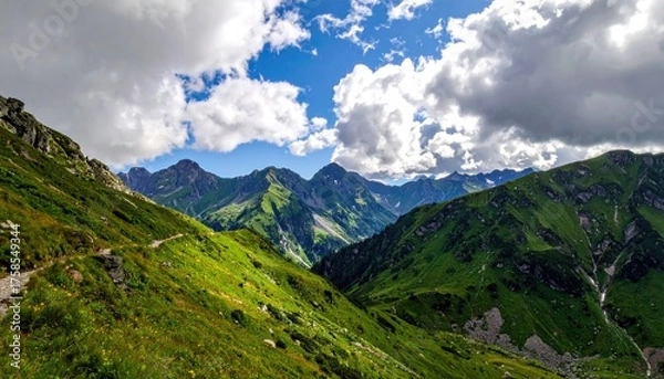 Fototapeta Lush Green Mountain Range With Rocky Peaks Under a Cloudy Blue Sky On a Sunny Day With a Winding Dirt Path in the Foreground