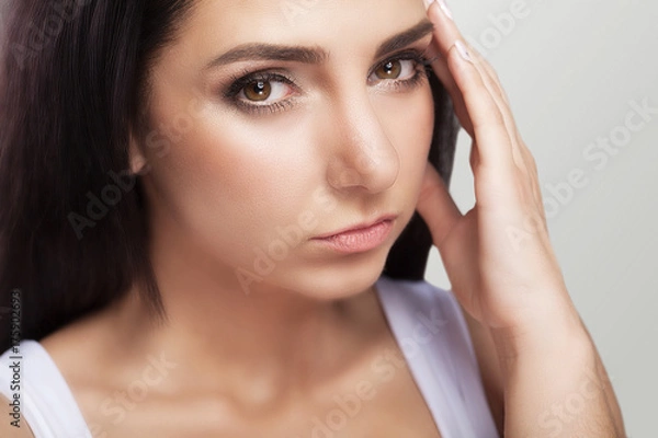 Obraz A tired, exhausted young woman who suffers from a severe headache of tension. Sufferers from headache. Migraines A sense of pressure and stress. On a gray background.