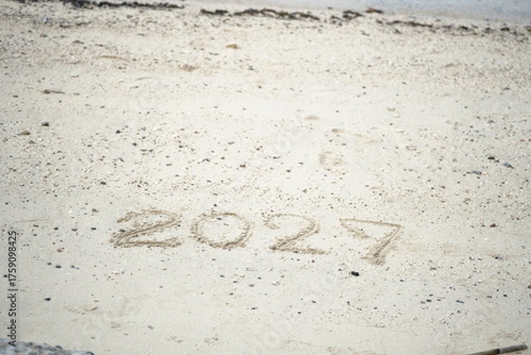 Fototapeta The number 2027 written on sandy beach under bright sunlight, symbolizing new beginnings, travel, and the coming future