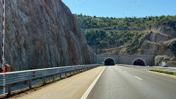 Fototapeta Sunlit highway tunnels burrow through rocky cliffs, echoing traveler's wanderlust and Earth Day's ode to nature's marvels