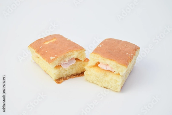 Fototapeta Close-up of sponge cake cut in half with pink cream filling, minimal food photo on white background, soft texture dessert for bakery, snack, or sweet breakfast concept.