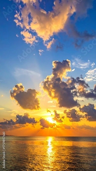 Fototapeta Vivid depiction of a coastal sunset. Dramatic clouds are backlit by the setting sun's golden rays, reflecting on the calm water