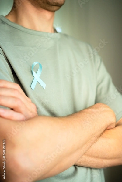 Obraz Close up of man with blue satin ribbon on shirt and crossed arms. Symbol of prostate cancer awareness month in November, self check, diagnosis, and timely medical treatment.