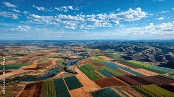 Obraz Aerial view of expansive colorful patchwork farmland with cultivated fields, vibrant crop patterns, distant rolling hills, blue sky with scattered clouds, scenic rural landscape