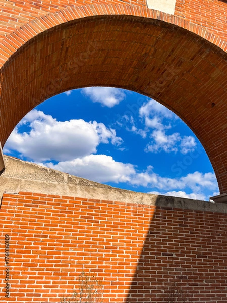 Fototapeta Red brick arch framing vivid blue sky and clouds